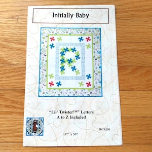 May include: A sewing pattern titled "Initially Baby" with a quilt design. The quilt features a large letter "R" made of blue and green shapes. The pattern includes "Lil' Twister Letters" and measures 57" x 50".