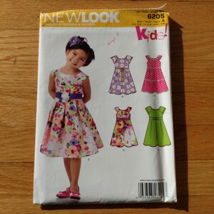 以下が含まれることがあります： 子供用ドレスのNew Look型紙6205。封筒には、紫色のサッシュが付いた花柄のドレスを着た子供の写真と、チェック柄、水玉模様、無地の緑色など、4種類のドレスデザインのイラストが掲載されています。