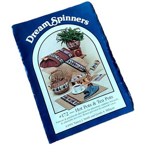 May include: A blue book titled "Dream Spinners" featuring a patchwork design for hot pots and tea pots. The cover displays various items, including a teapot, placemats, and a teacup. The text reads "#172 - Hot Pots & Tea Pots."