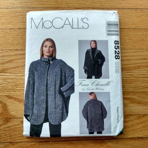May include: McCall's sewing pattern for a faux chenille cape. The pattern features a woman wearing the cape in two different views. The pattern number is 8528. The cape is a dark grey colour.