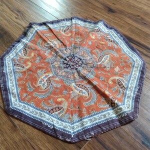Peut inclure: Un tapis en tissu octogonal présentant un fond orange vif avec un motif détaillé de cachemire et de fleurs dans des tons de bleu, crème et brun foncé. La bordure se compose d'une bande décorative crème et brune avec un motif floral répétitif.