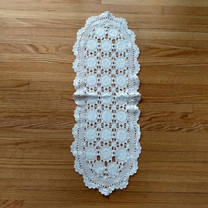Peut inclure: Chemin de table ovale en dentelle blanche avec bordure festonnée. Le chemin de table présente un motif répétitif de médaillons floraux et de détails ajourés, idéal pour ajouter une touche de charme vintage.