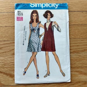 May include: A vintage Simplicity sewing pattern, number 8283, showing two women in dresses. One is a white dress with black polka dots, the other a burgundy jumper over a turtleneck. The pattern is for Miss size 16, bust 96.5 cm.