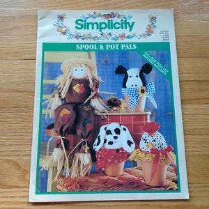 May include: Simplicity Spool & Pot Pals pattern. The cover features a scarecrow, a cow, a Dalmatian, and a chicken, all crafted to sit atop pots. The scarecrow has a straw hat and brown clothing. The cow has a blue and white checkered bow.