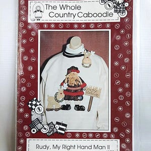 May include: A craft pattern packet titled The Whole Country Caboodle Rudy, My Right Hand Man II #133. The cover features a white long-sleeve shirt with a fabric applique of a bearded figure and a reindeer, plus a small reindeer pin accessory.