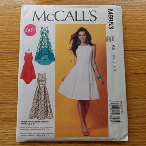 May include: McCall's sewing pattern M6953 for dresses. The pattern features a woman in a white dress and illustrations of other dress designs. The package includes the size A5 (6-8-10-12-14) and the word "EASY".