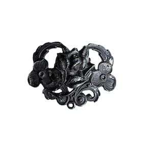 May include: A dark gray metal brooch with a floral design. The brooch features a central rose surrounded by leaves and two stylized flowers. The design includes decorative swirls and a curved frame.