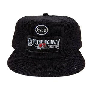 May include: Black corduroy baseball cap featuring the Esso logo and the phrase "KEY TO THE HIGHWAY" on a patch. The cap has a structured crown and a curved brim. The patch depicts a red truck.