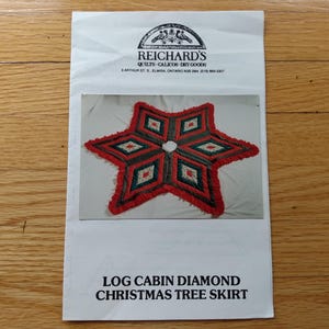 May include: A white paper pattern envelope labelled REICHARD'S QUILTS-CALICOS-DRY GOODS and LOG CABIN DIAMOND CHRISTMAS TREE SKIRT. The envelope features a photograph of a six-pointed star-shaped tree skirt with red, green, and white diamond patterns.