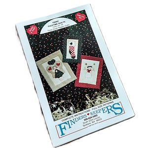 May include: A rectangular sewing pattern packet titled Teeny Yuletime Quilts, Pattern No. 106. The cover features three small raggy quilts with holiday designs, including a stocking, a snowman, and a figure, set against a black background with dots.