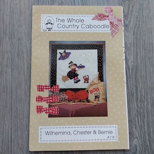 May include: A craft pattern booklet titled The Whole Country Caboodle featuring Wilhemina, Chester & Bernie #118. The cover displays a Halloween-themed quilt design with a witch, a cat, a pumpkin, and a bag labeled BOO, accented by red gingham bows.