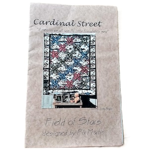 May include: A printed paper with the title "Cardinal Street" and the quote "It seams we all needle little friendship sew." The image features a quilt design with red and blue stars. The text "Field of Stars" and "designed by Pix Martin" are also visible.