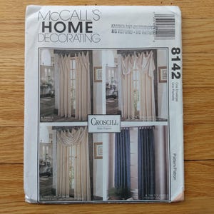 May include: A vintage McCall's Home Decorating pattern. The pattern features illustrations of various curtain styles, including panels and valances. The cover includes the number 8142 and the CrosCill brand name. The background is a wooden surface.
