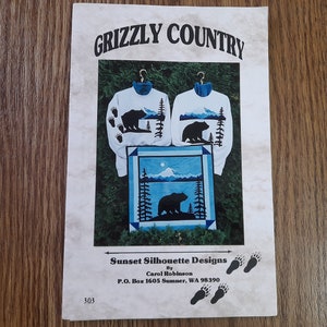 May include: A paper pattern booklet titled GRIZZLY COUNTRY featuring two white sweatshirts with blue collars and black bear silhouettes, plus a square quilt design showing a bear, trees, and a mountain. Text includes Sunset Silhouette Designs.