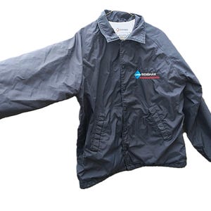 May include: A dark gray jacket with a collar and two front pockets. The jacket has a zipper closure and the text "BENSHAW" is printed on the right chest area. The jacket is made of a lightweight material.