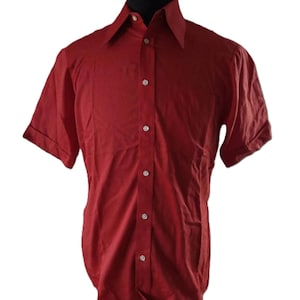 May include: A short-sleeved, button-down shirt in a deep red colour. The shirt features a classic collar, a chest pocket, and is buttoned up. The sleeves are cuffed, and the shirt is displayed on a black mannequin.