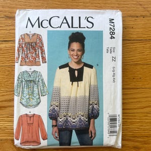 Peut inclure: Une pochette de patron de couture McCall's M7284 présentant des illustrations de quatre tuniques à manches longues différentes. Les modèles incluent divers motifs floraux et géométriques en orange, bleu sarcelle et crème, avec une image centrale d'une personne portant une tunique crème et noire.