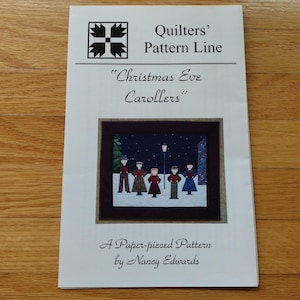 May include: A paper-pieced quilting pattern titled "Christmas Eve Carolers" by Nancy Edwards. The cover features a square image of carolers under a lamppost. The pattern is from the Quilters' Pattern Line.