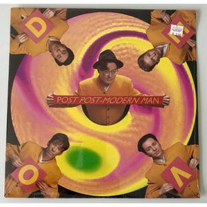 May include: Album cover featuring a group of men in yellow suits and hats, with the text "POST POST-MODERN MAN" on a banner. The background has a swirling pattern of yellow, pink, and purple.