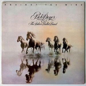 May include: A square vinyl record cover featuring the text Against The Wind, Bob Seger & The Silver Bullet Band. The artwork depicts five horses galloping through shallow water, creating splashes and reflections against a soft, hazy background.
