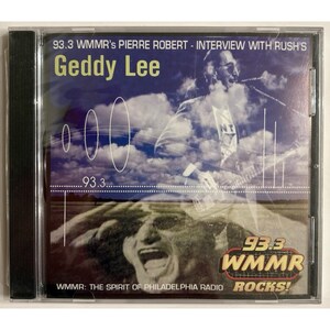 May include: A CD case featuring Geddy Lee, with text indicating an interview by Pierre Robert on 93.3 WMMR. The cover art includes a photo of Geddy Lee and a radio graphic. The CD case is in a clear plastic case.