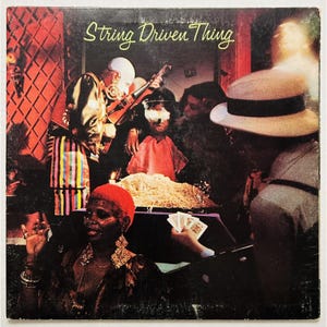 May include: Album cover for "String Driven Thing" featuring a group of people in a dimly lit room. The cover art includes a person playing a guitar, a person wearing a hat, and a person holding playing cards. The album title is in green text.