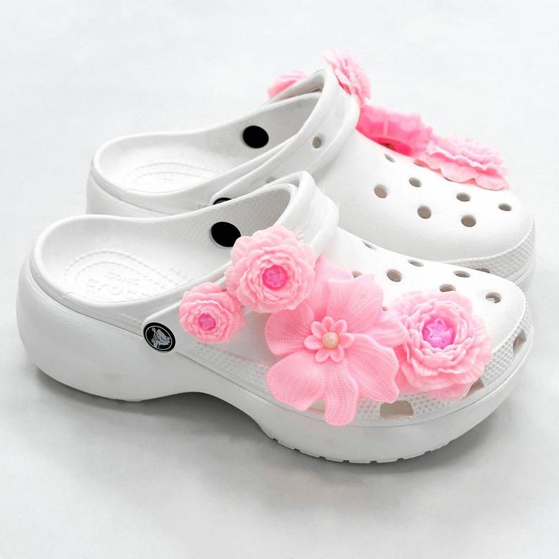 Pu&ograve; includere: Zoccoli bianchi decorati con decorazioni floreali rosa. Gli zoccoli hanno una suola spessa e un cinturino che pu&ograve; essere indossato attorno al tallone o sopra il piede. Le decorazioni floreali includono diversi fiori piccoli e un fiore pi&ugrave; grande.