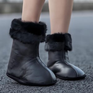 Puede incluir: Botines de cuero negro con ribete de piel. Los botines tienen punta redonda y suela plana. Los botines se muestran en los pies de una persona.