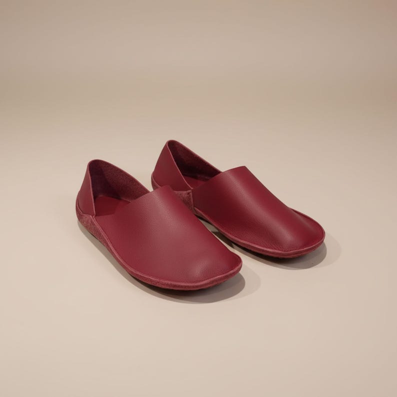 May include: A pair of burgundy leather slip-on shoes. The shoes have a rounded toe and a low profile, with a simple, minimalist design. The leather appears smooth and the color is a deep, rich red.
