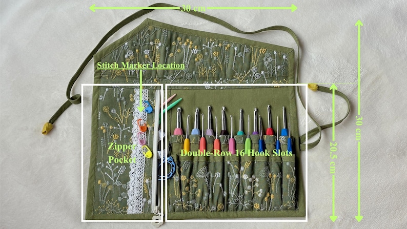 Puede incluir: Un organizador de tela verde oliva con bordado floral, que cuenta con un bolsillo con cremallera para marcadores de puntos y una secci&oacute;n de doble fila con 16 ranuras para ganchillos. El organizador mide 30 cm de ancho por 30 cm de alto.