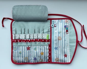 Peut inclure: Un étui en tissu pour crochets de couleur bleu clair avec une bordure rouge. L'intérieur présente des poches à rayures bleues et blanches ornées de coquillages et d'étoiles de mer, une bordure en dentelle blanche, une poche zippée et des crochets.