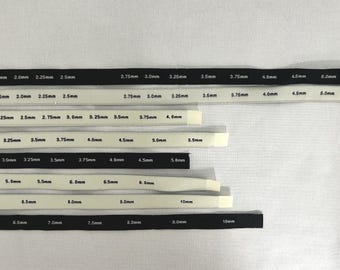 Peut inclure: Un ensemble de huit bandes de mesure flexibles en noir et blanc, chacune imprimée avec diverses tailles métriques allant de 1,5 mm à 10 mm. Ces bandes sont conçues pour identifier les diamètres d'aiguilles ou de crochets, avec un texte clair.