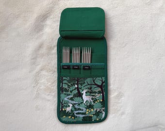 Peut inclure: Un étui en tissu vert foncé contenant trois jeux d'aiguilles à tricoter métalliques. L'étui possède un rabat et une poche inférieure ornée d'un motif de forêt avec des cerfs, des arbres et un ruisseau. Des étiquettes indiquent 3,5 mm, 4,5 mm et 5,5 mm.