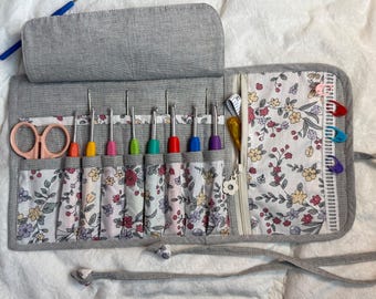 Peut inclure: Un étui de rangement en tissu gris avec des crochets colorés, une paire de ciseaux rose clair et une poche zippée à motif floral. L'étui est doté d'une fermeture à nouer et contient plusieurs marqueurs de mailles en plastique.