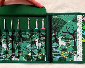 Peut inclure: Un étui de rangement en tissu vert foncé pour crochets, orné d'un motif de forêt avec des cerfs blancs, des arbres et des fleurs jaunes. L'étui comprend sept emplacements pour crochets en métal et un panneau latéral avec dentelle blanche.