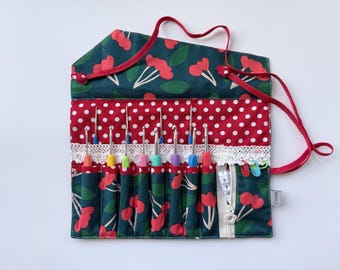 Peut inclure: Un étui à crochets en tissu avec un motif de cerises sur fond vert foncé, une bande à pois rouges et blancs et une bordure en dentelle blanche. Il contient huit crochets colorés, un mètre ruban blanc et deux marqueurs de mailles, avec des liens rouges.