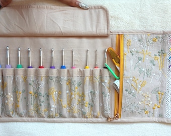 Peut inclure: Un organisateur en tissu beige enroulable avec un motif floral brodé en jaune et vert. Il contient onze crochets en métal avec des manches colorés, une poche zippée jaune et quatre marqueurs de mailles en plastique rose, jaune, bleu et violet.
