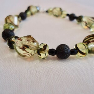 May include: A green and black beaded necklace with lava rock beads. The necklace is made with glass beads with a brown and green swirl pattern.