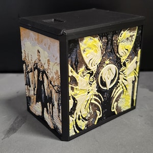 May include: A black, rectangular box with a hinged lid. The sides feature detailed, raised artwork in yellow, brown, and white, depicting figures and abstract designs. The box appears to be 3D-printed.