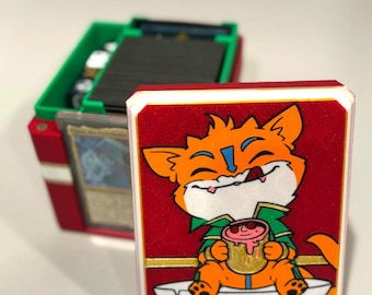 May include: A red and white card case with a cartoon fox illustration holding a mug. The case is open, revealing a green and red card storage box filled with cards. The case has a gold border.