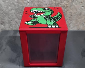 May include: A red box with a transparent front panel. The top of the box features a green cartoon dinosaur illustration. The dinosaur is running and has white accents. The box is likely for storage or display.