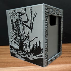 May include: A gray, rectangular box with a detailed black illustration of a creature with multiple arms and a city silhouette. The box has a decorative border and a cutout on one side, likely for storage.