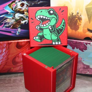May include: A red card storage box with a green dinosaur graphic on the lid. The box is open, revealing a stack of green cards. Other boxes with colorful artwork are in the background.