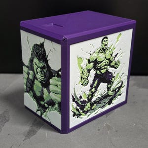 May include: A purple rectangular storage box featuring embossed white panels on the front and side. The side panel displays a close-up of the Hulk's face, while the front panel shows a full-body illustration of the Hulk in a dynamic pose.