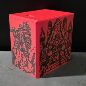 May include: A bright red rectangular storage box featuring black engraved illustrations on two sides. One side depicts a standing figure holding a large hammer, while the other side shows a seated figure with a hammer on a throne-like structure.