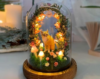 Puede incluir: Una cúpula de cristal decorativa con una figura de gato rodeada de flores y setas iluminadas. La base es de madera. La palabra "Chloe" está escrita en un pequeño letrero dentro de la cúpula. La escena está iluminada con luces cálidas y suaves.