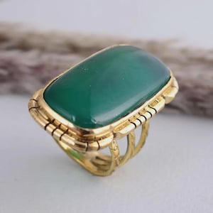 May include: A gold-toned ring featuring a large, rectangular, emerald-green stone. The ring has a detailed, textured band and a decorative setting around the stone. The ring's design is vintage-inspired.