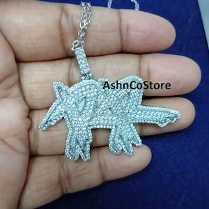 May include: Silver-colored pendant necklace with a large, ornate pendant. The pendant is encrusted with small, sparkling stones, and features a stylized design. The necklace is displayed against a blue background.