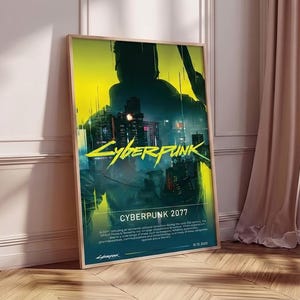 Op de afbeelding: Een ingelijste poster met de titel "Cyberpunk 2077" in geel en groen, met een futuristisch stadsbeeld. De poster zit in een houten lijst en leunt tegen een muur. Het kleurenschema is donker met neonaccenten.