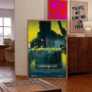 Op de afbeelding: Een ingelijste poster met de tekst "Cyberpunk 2077" in geel, met een silhouet en een stadsgezicht. De poster heeft een houten lijst en wordt op een houten vloer getoond. Andere ingelijste kunstwerken zijn zichtbaar op de achtergrond.